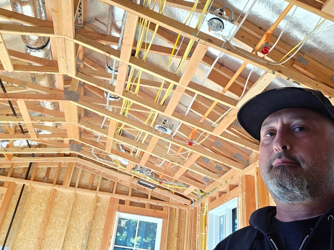 Man in a black cap standing in a framed house under construction with exposed rafters overhead