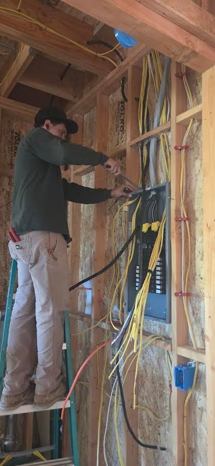 Worker on a ladder wiring a wall frame inside an unfinished house.