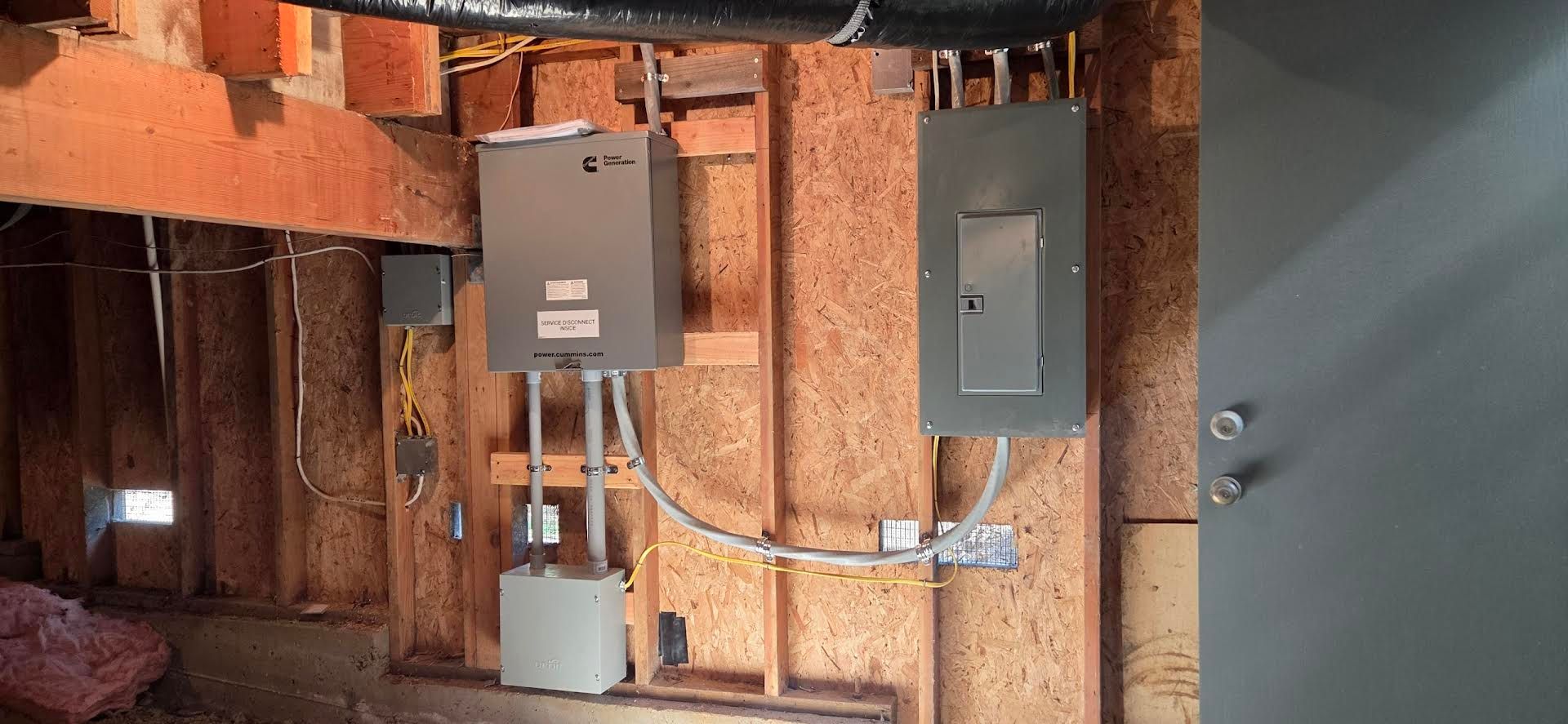 Electrical panels and conduit mounted on plywood wall inside a construction area