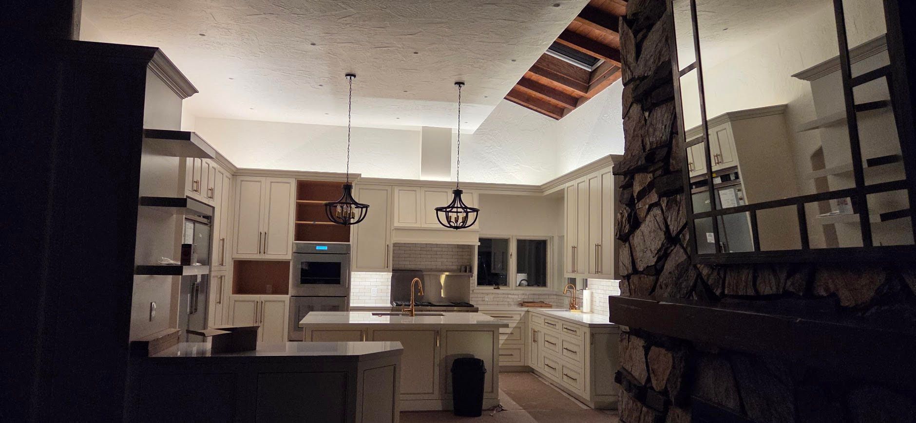 Dim kitchen interior with white cabinets, island, pendant lights, and a dark countertop in the foreground