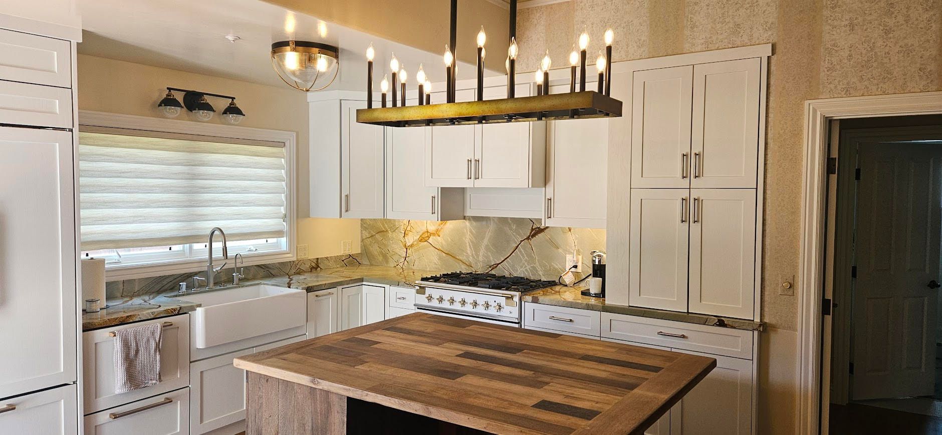 Bright kitchen with island, white cabinets, wood countertops, and a black chandelier under a vaulted ceiling