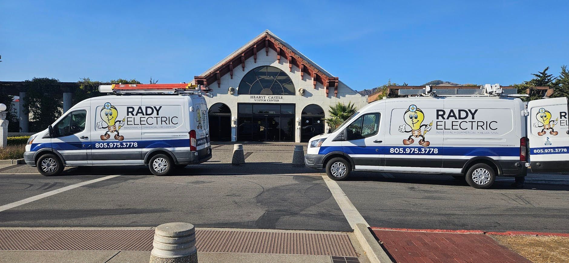 Two white and blue Baby Tractor vans parked in front of a building with arches