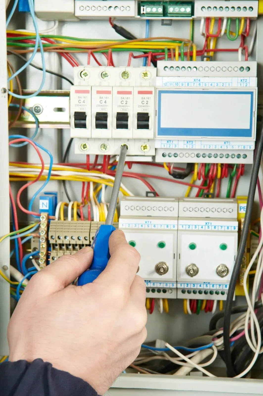 Hand with screwdriver working on a control panel with wires and circuit breakers.