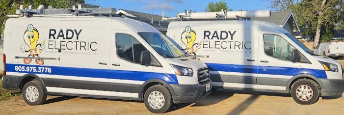 Two rady electric vans are parked next to each other on a dirt road.