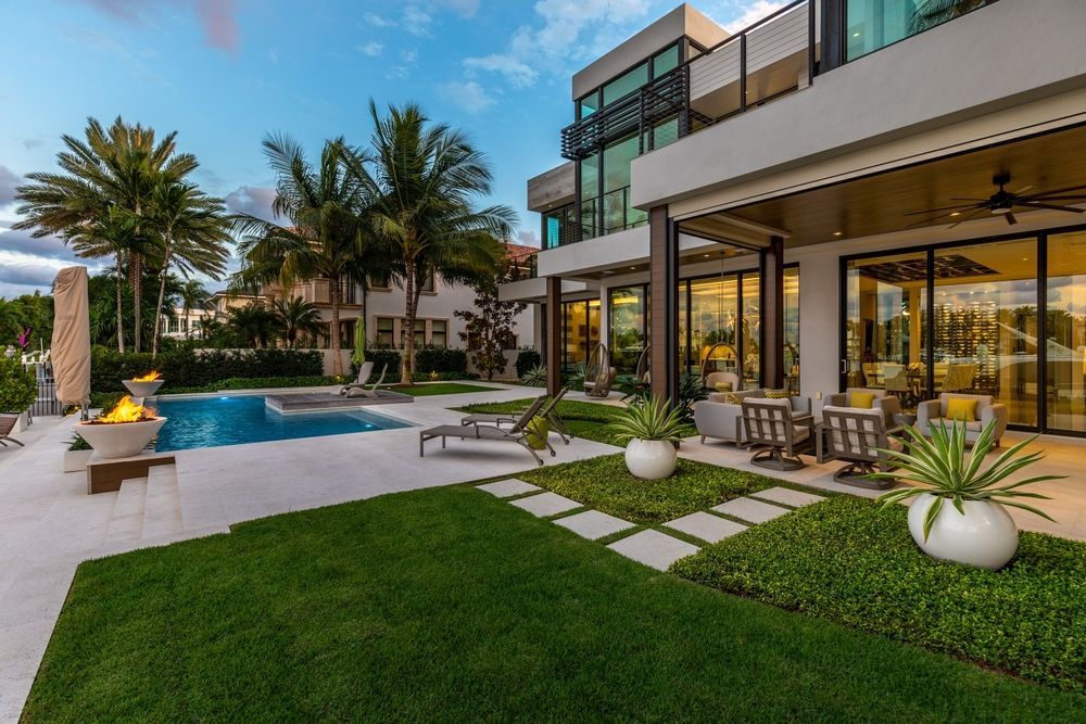 Modern luxury house patio with pool, palm trees, and glass walls at dusk