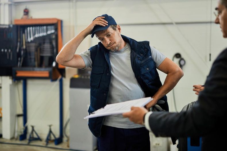 Worker in a warehouse holding his head while discussing papers with a colleague