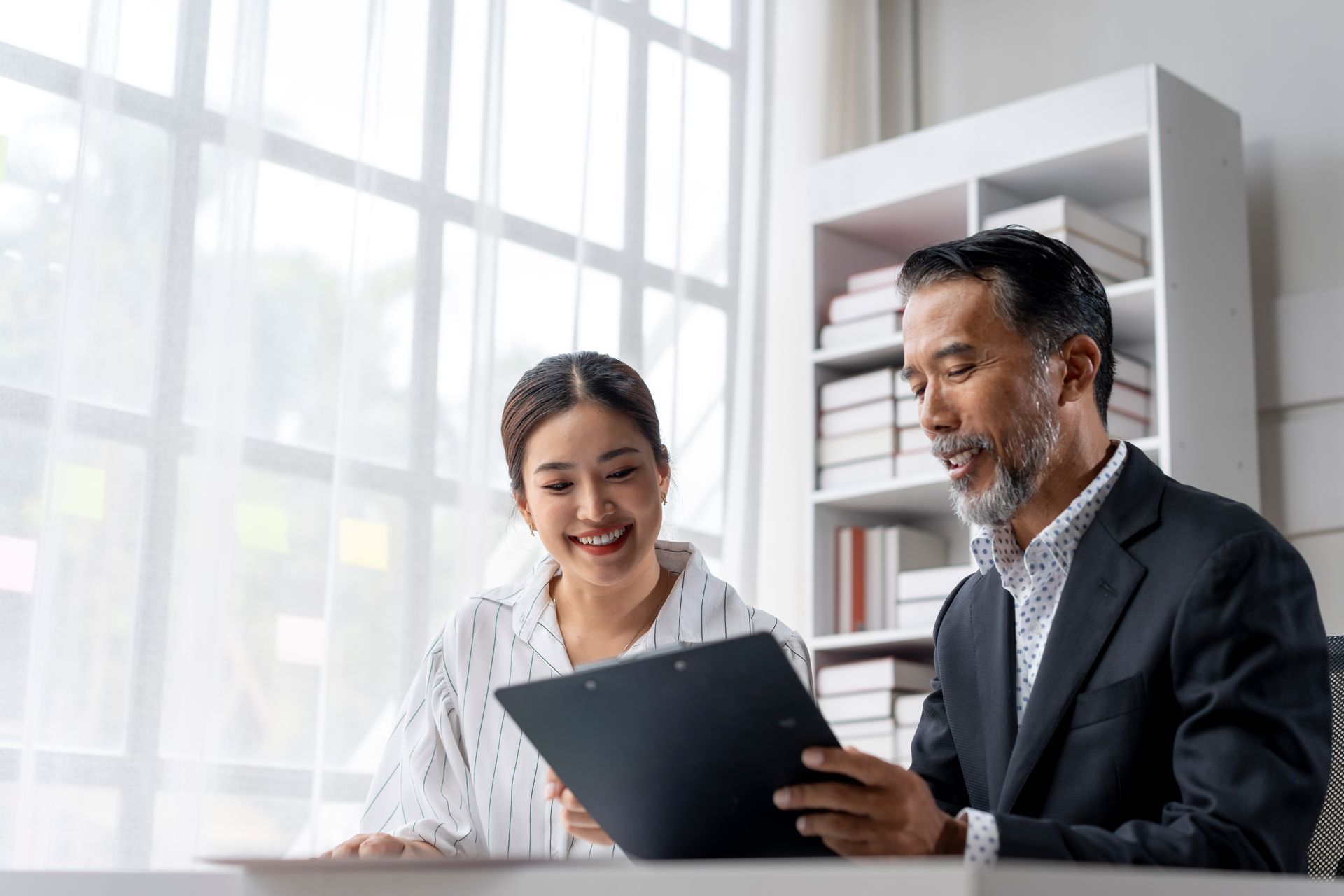 Two coworkers reviewing a tablet in a bright office, smiling at a desk.