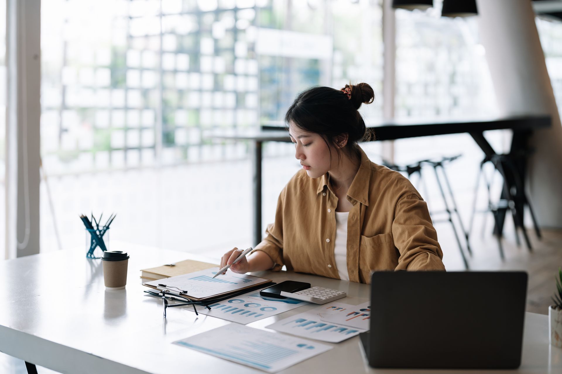 Person working at a desk with papers and a laptop in a bright office