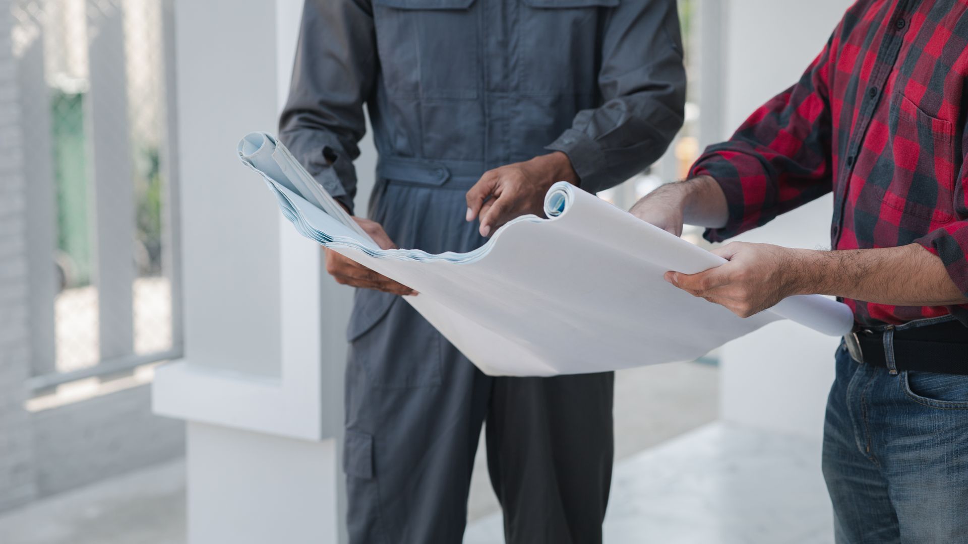 Two people holding and reviewing large white architectural plans indoors