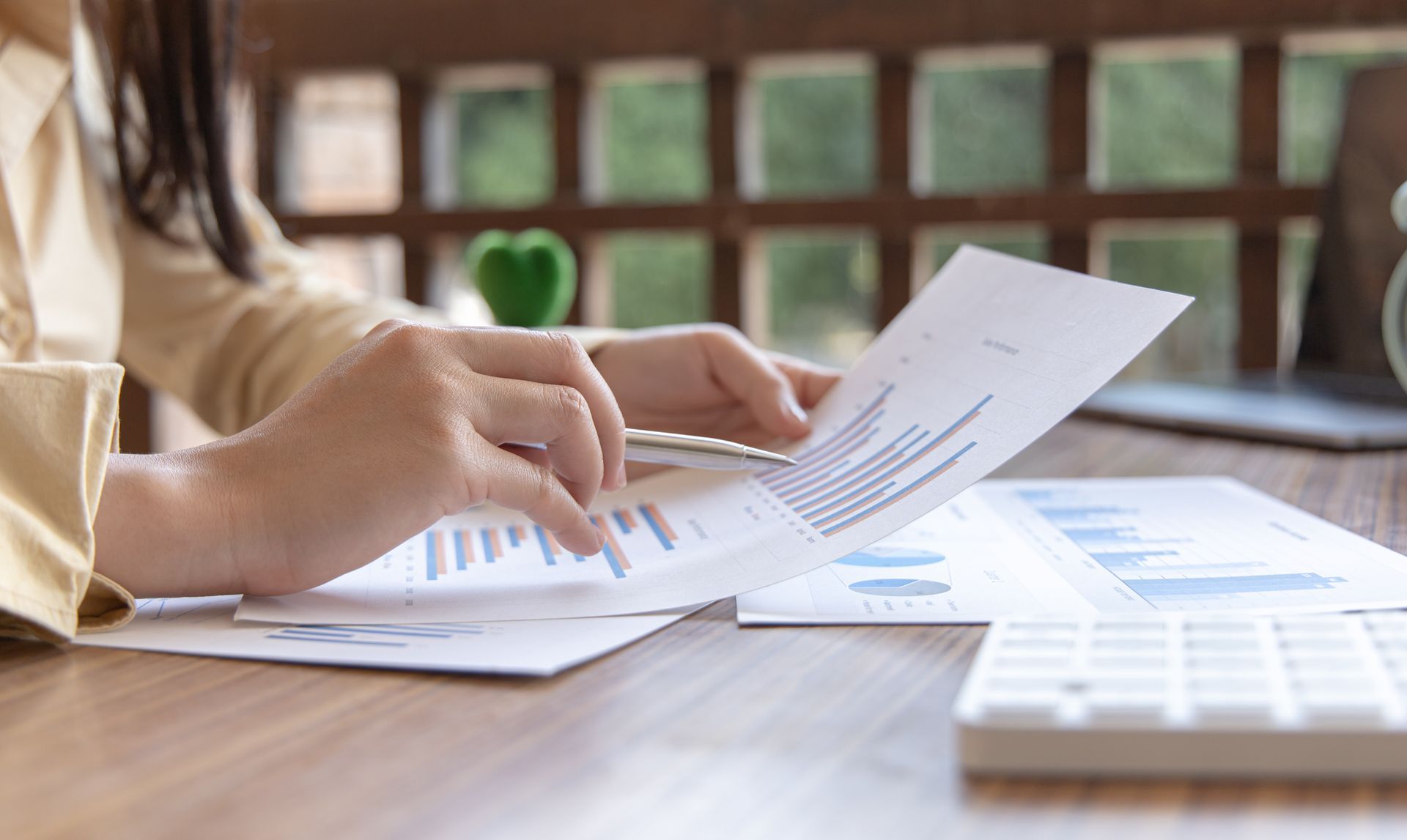 Hands reviewing printed documents at a wooden table with a calculator and laptop nearby
