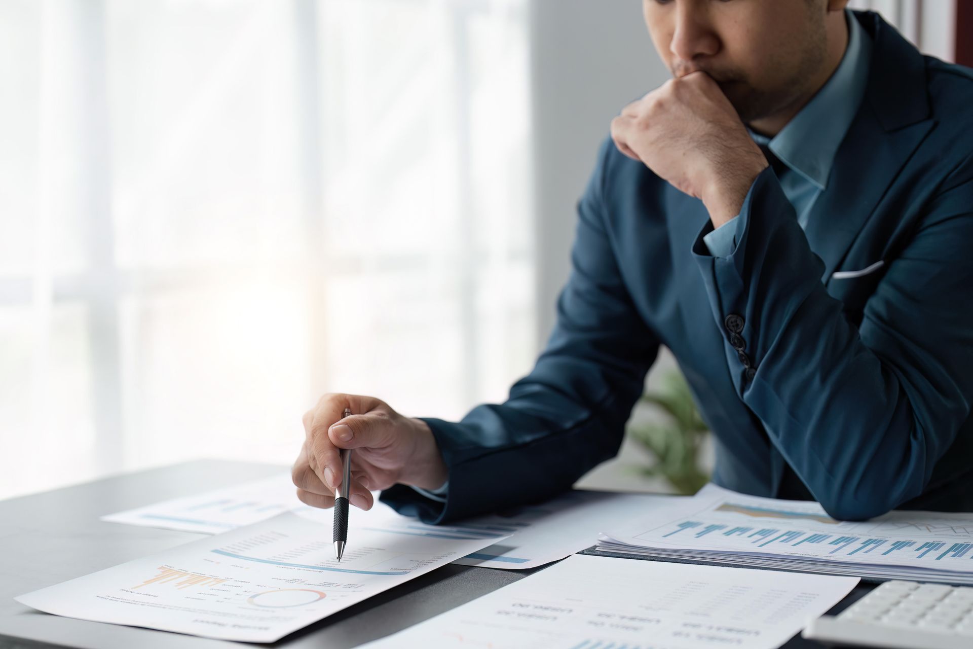 Person in a blue shirt reviewing documents and writing at a desk.