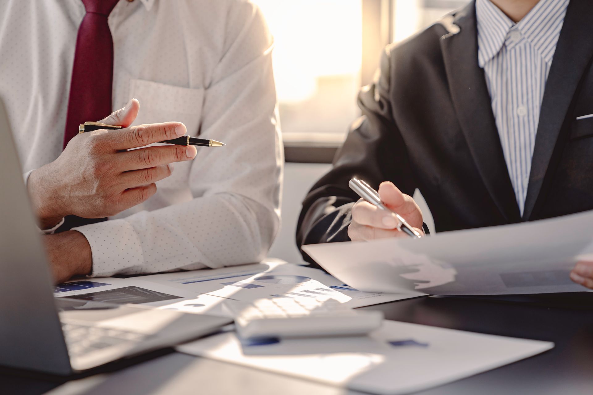 Two business people reviewing documents at a desk, one taking notes and one holding a smartphone