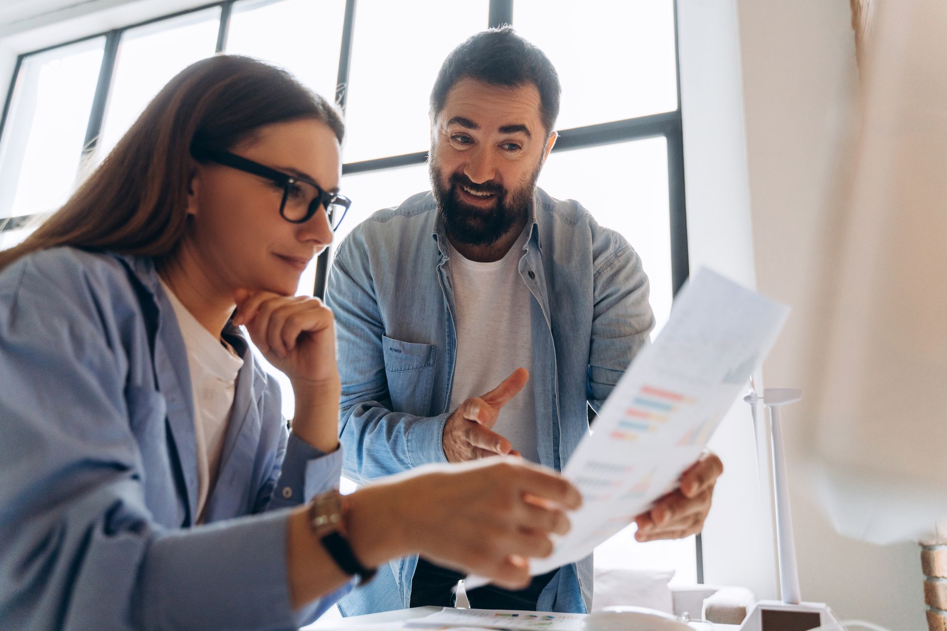 Two coworkers reviewing documents at a desk in a bright office