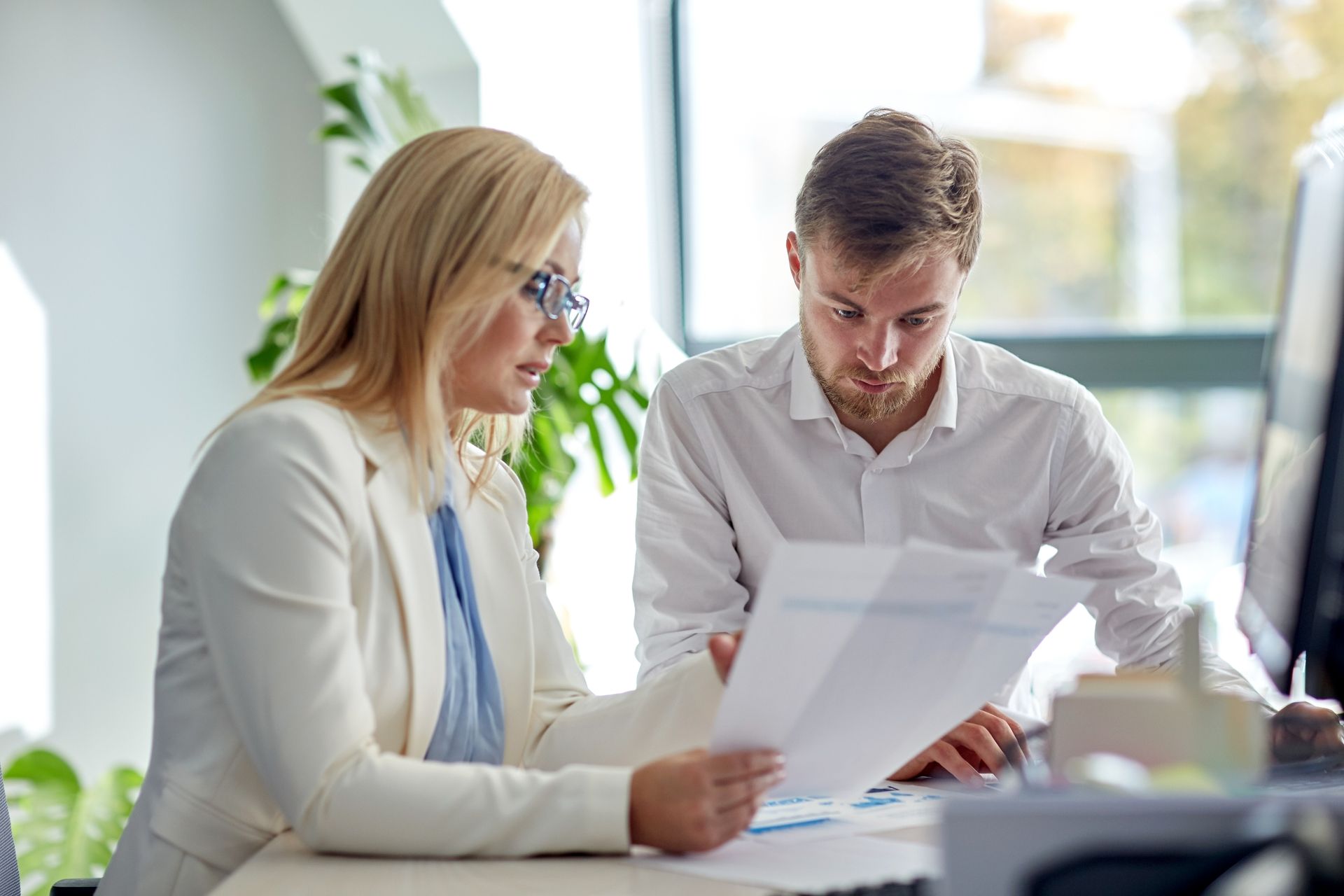 Two colleagues reviewing documents together at a desk in a bright office
