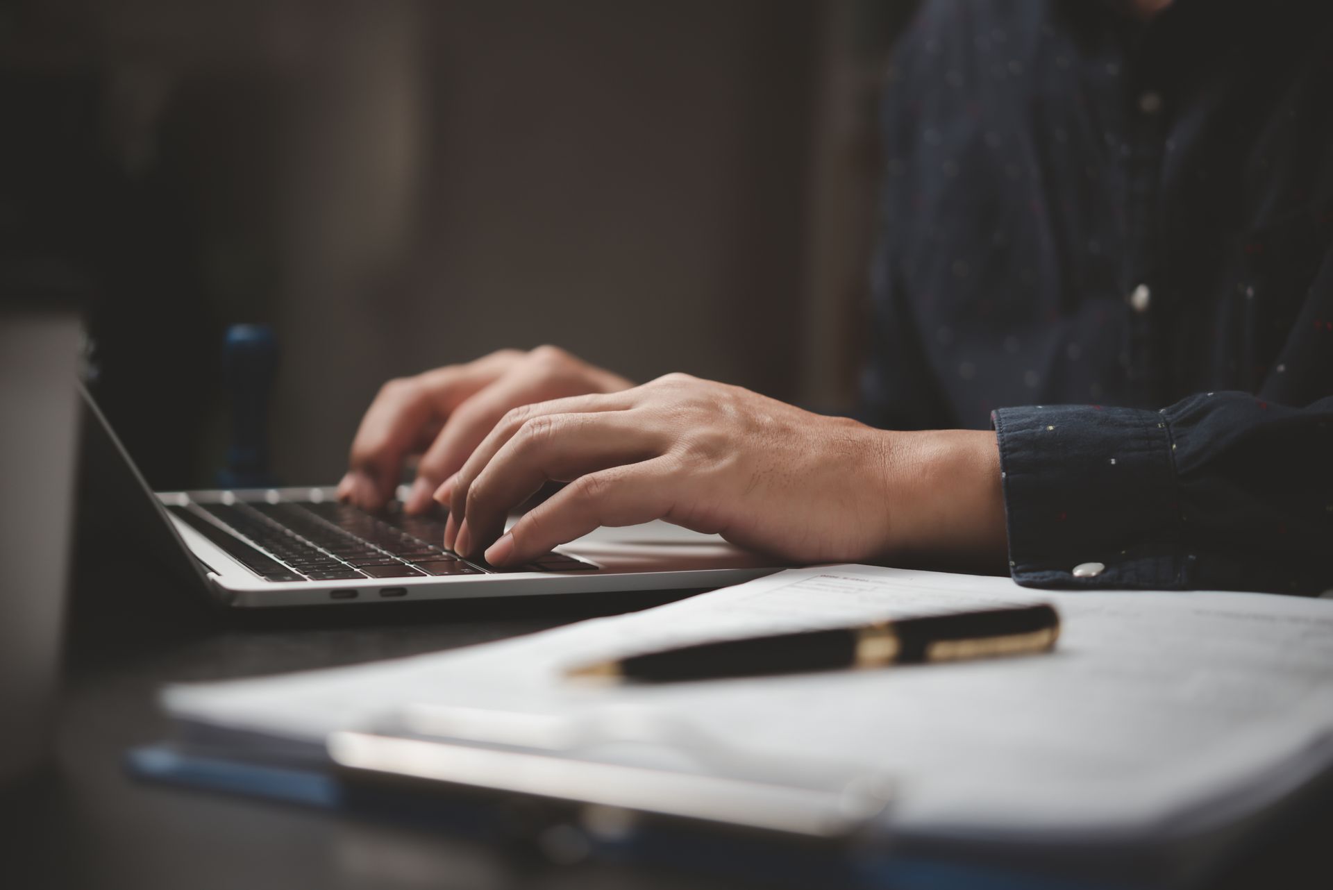 Hands typing on a laptop beside a pen and notebook on a desk