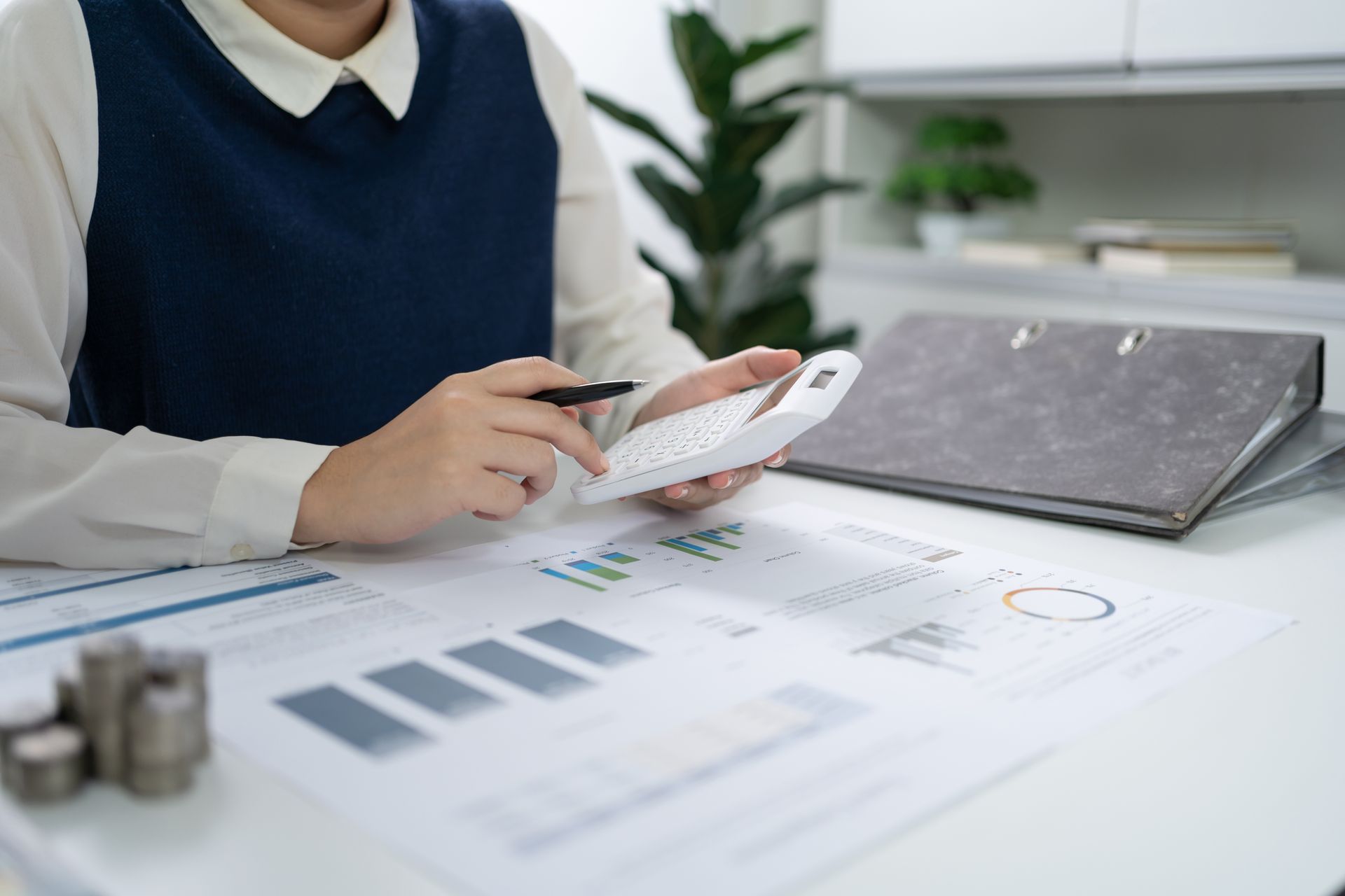 Person analyzing printed charts and holding a calculator at a desk in an office.