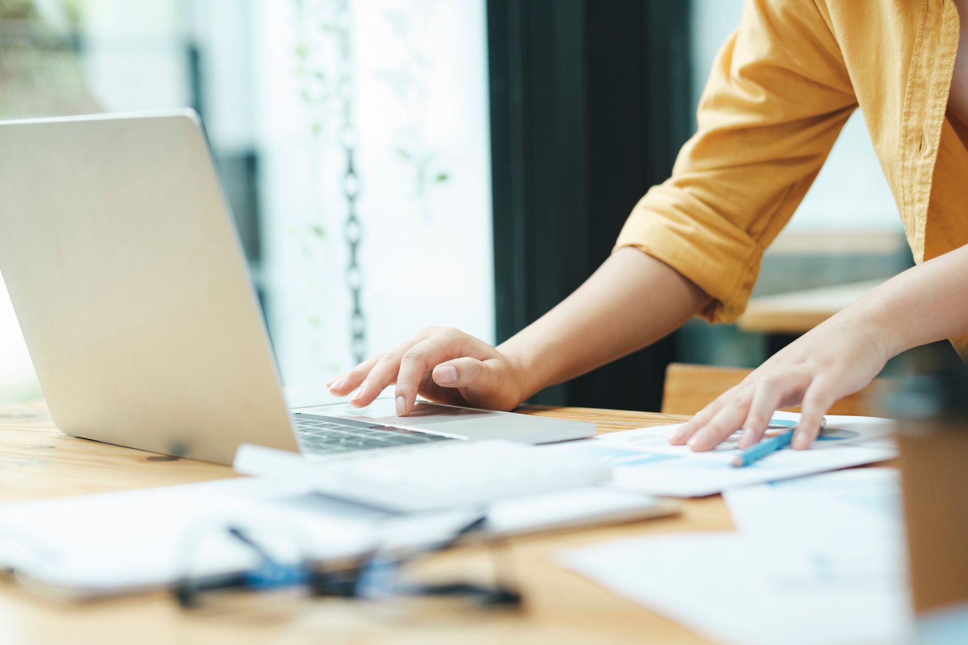 Person typing on a laptop at a desk with papers in a bright office