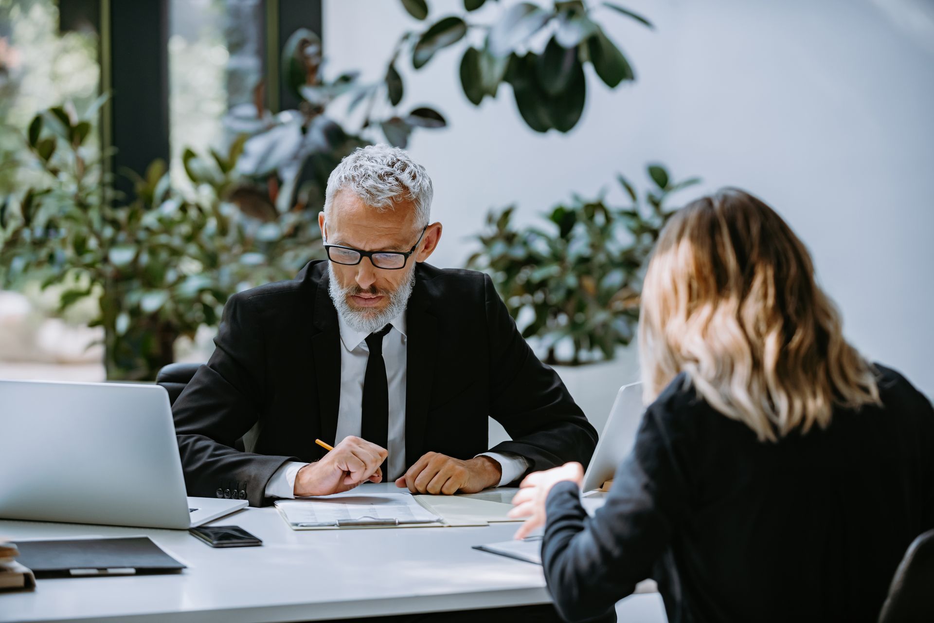 Two people in a meeting at a desk with a laptop and documents in a bright office.