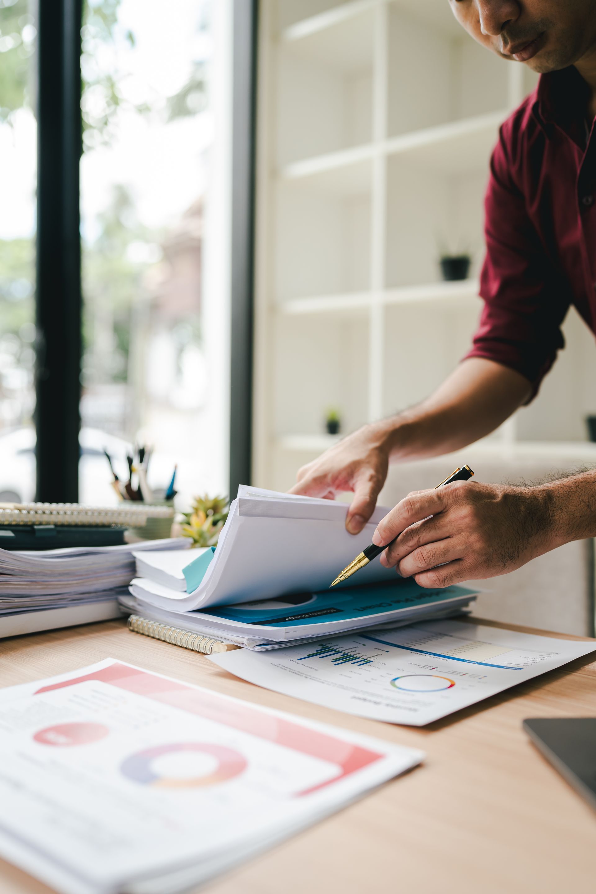 Person sorting papers on a desk beside charts and a laptop in an office