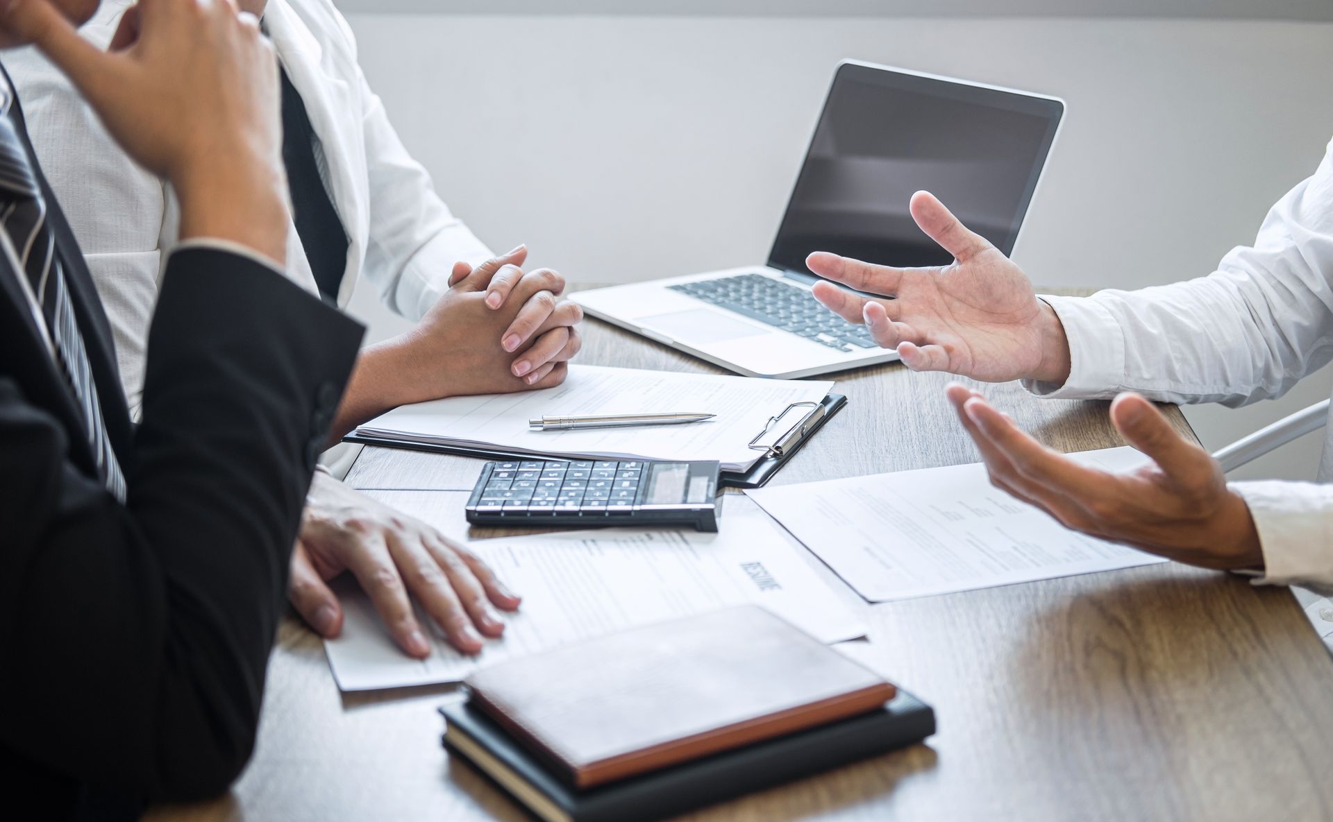 Business meeting with people discussing charts and documents around a conference table with a laptop and calculator