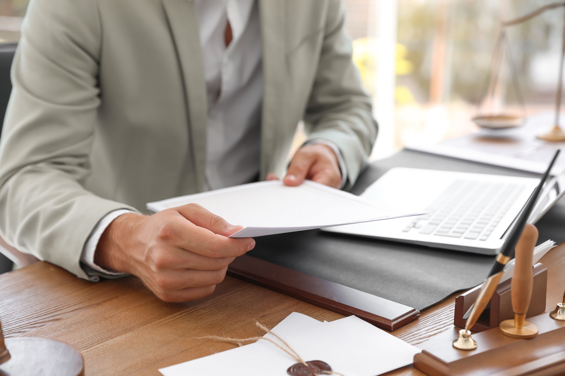 Person in a light suit reviewing papers at a desk with a laptop and scales of justice