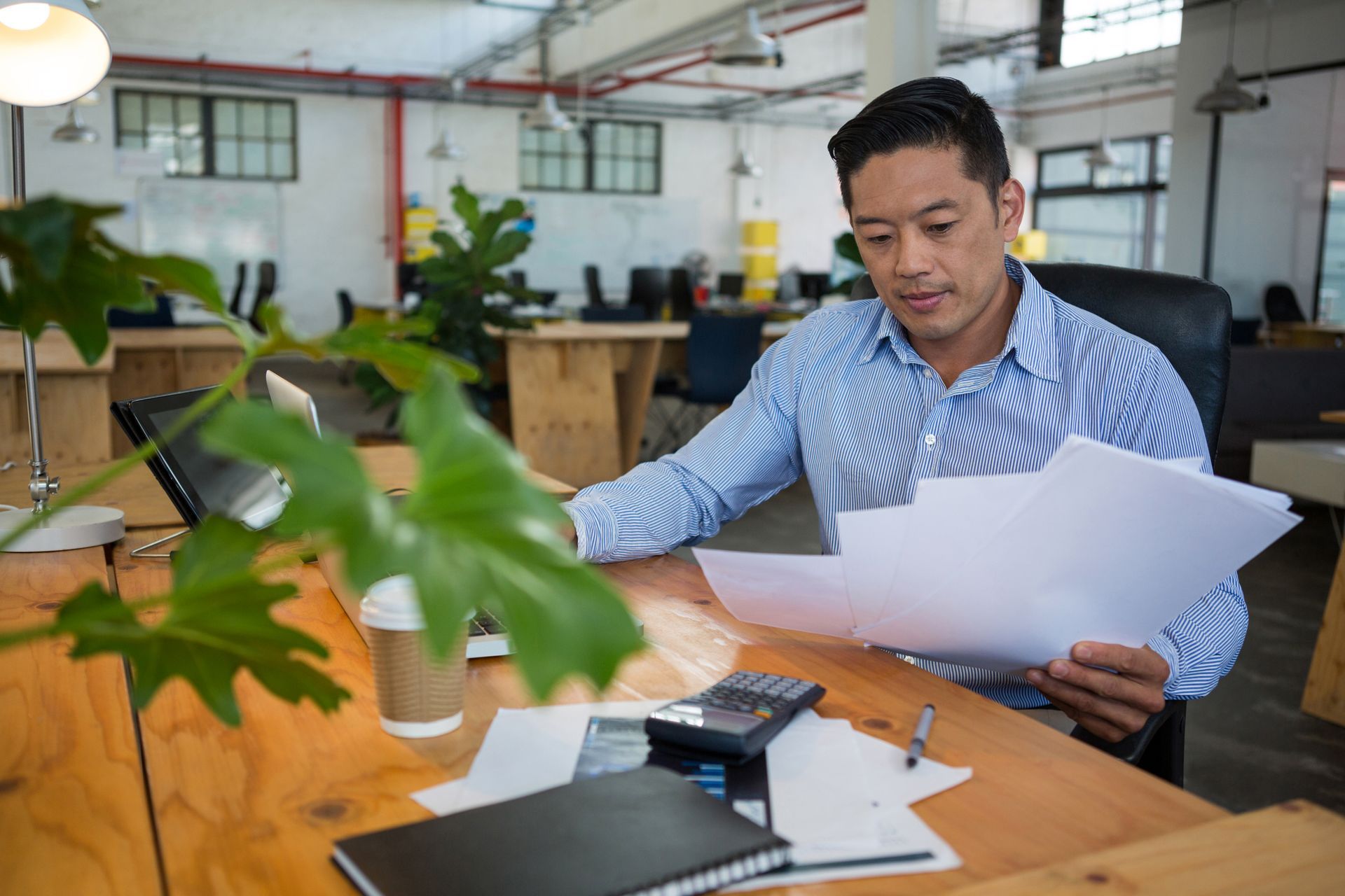 Man reviewing documents at a desk in a bright office with a laptop and office supplies