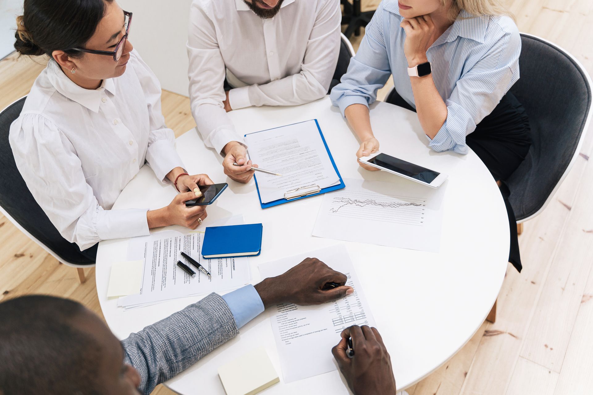 People gathered around a white table reviewing documents and a clipboard in a meeting.