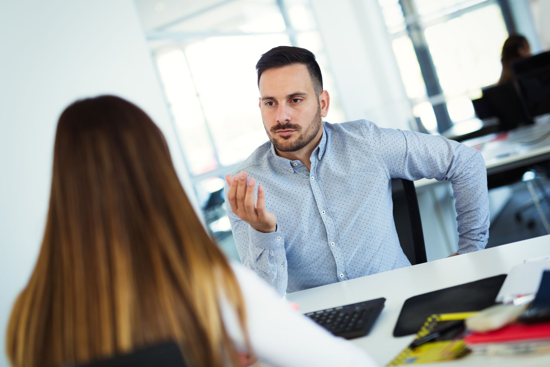 Office meeting with two people talking across a desk, laptops open on the table.