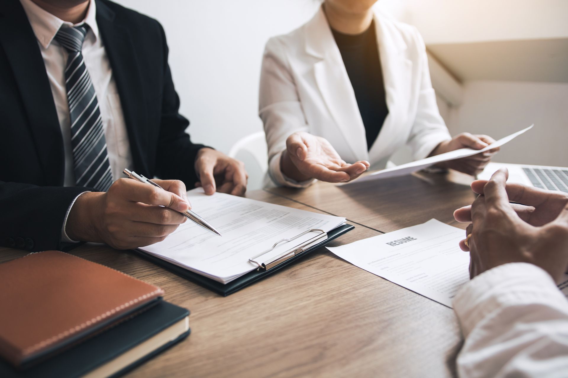 Business meeting at a conference table with notebooks, papers, and hands taking notes and discussing documents