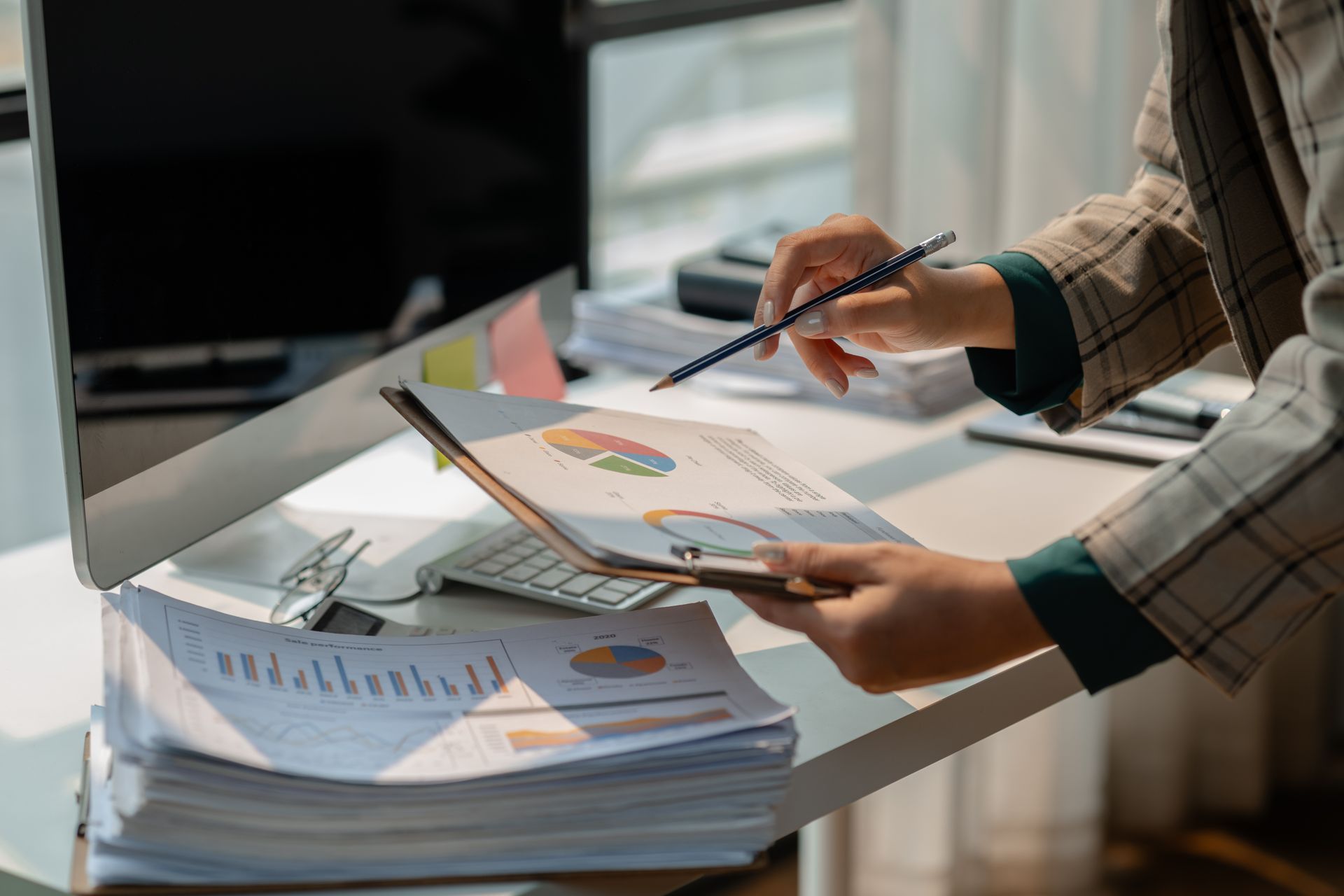 Hands reviewing printed charts and papers on a desk beside a laptop in a bright office