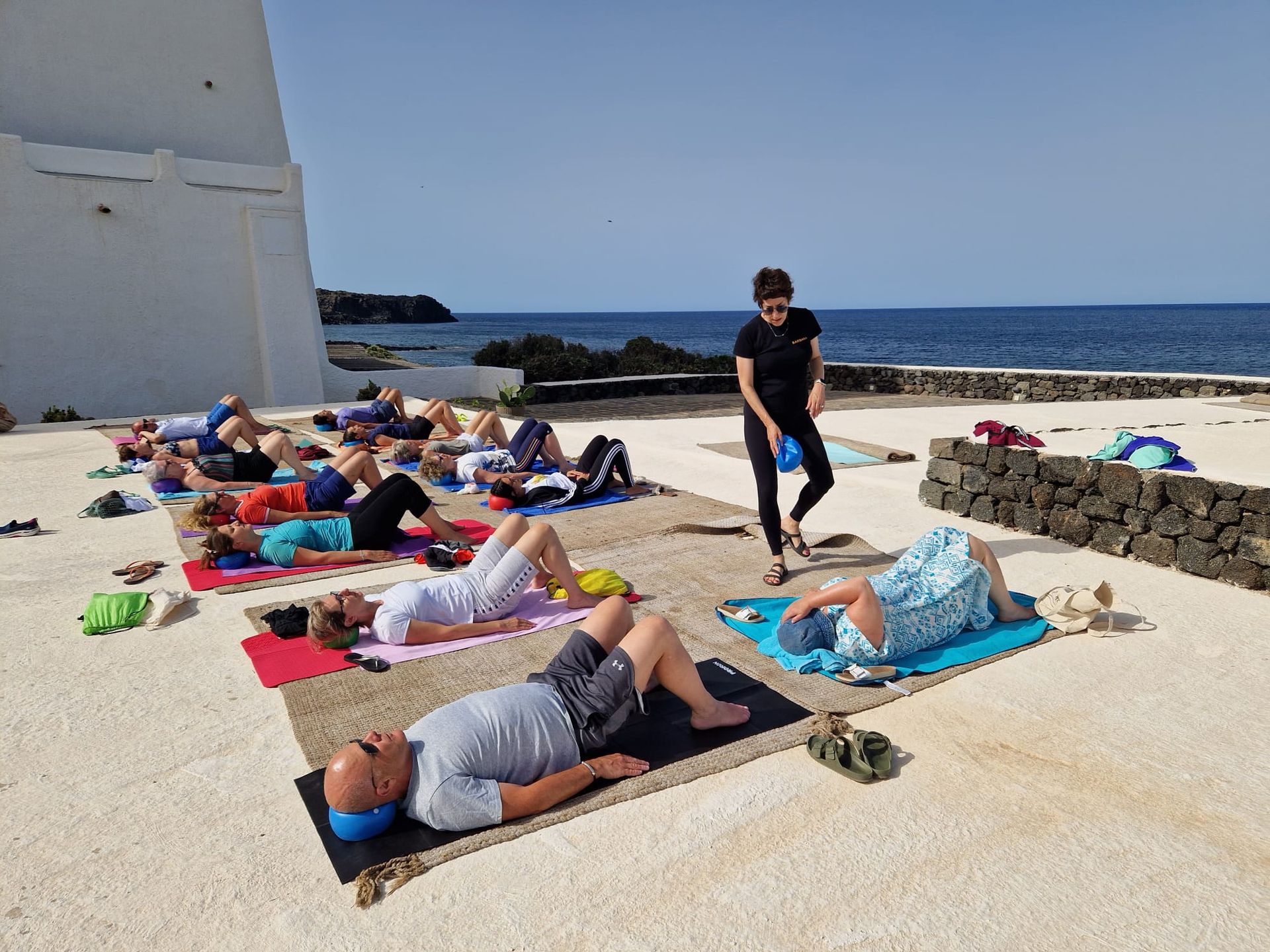 Persone che fanno yoga all'aperto su tappetini, istruite da qualcuno.