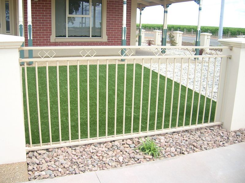 A fence surrounds a lush green lawn in front of a brick house