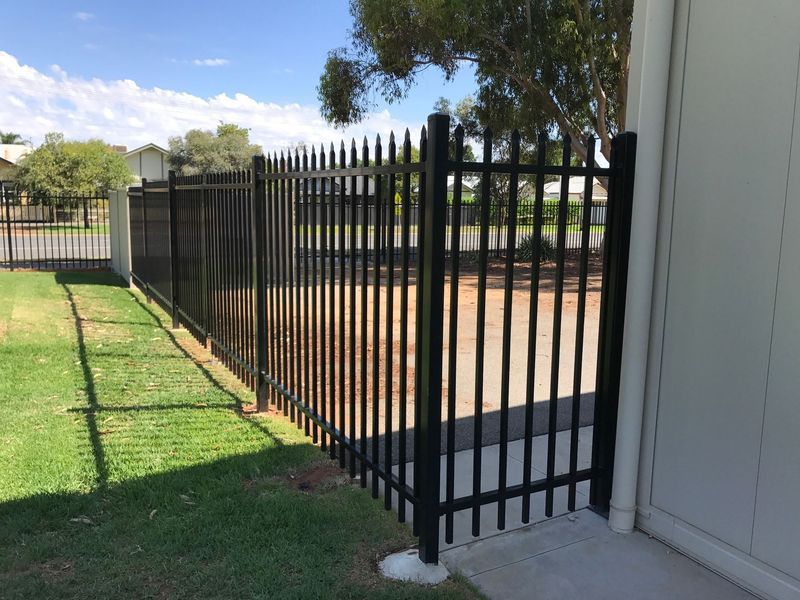 A black fence is surrounding a grassy area next to a building.