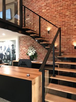 A wooden staircase with a glass railing in a room with a brick wall.