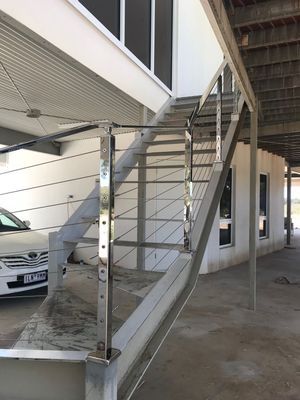 A car is parked under a staircase in a parking garage.