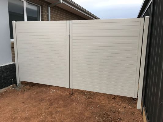 A white fence is sitting in the dirt in front of a house.