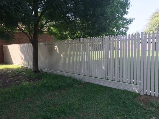 A white picket fence is surrounded by grass and trees in a backyard.