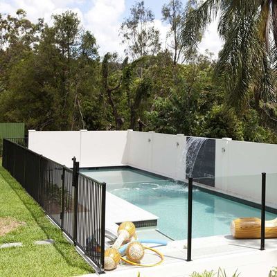 A swimming pool with a black fence and a waterfall in the backyard.