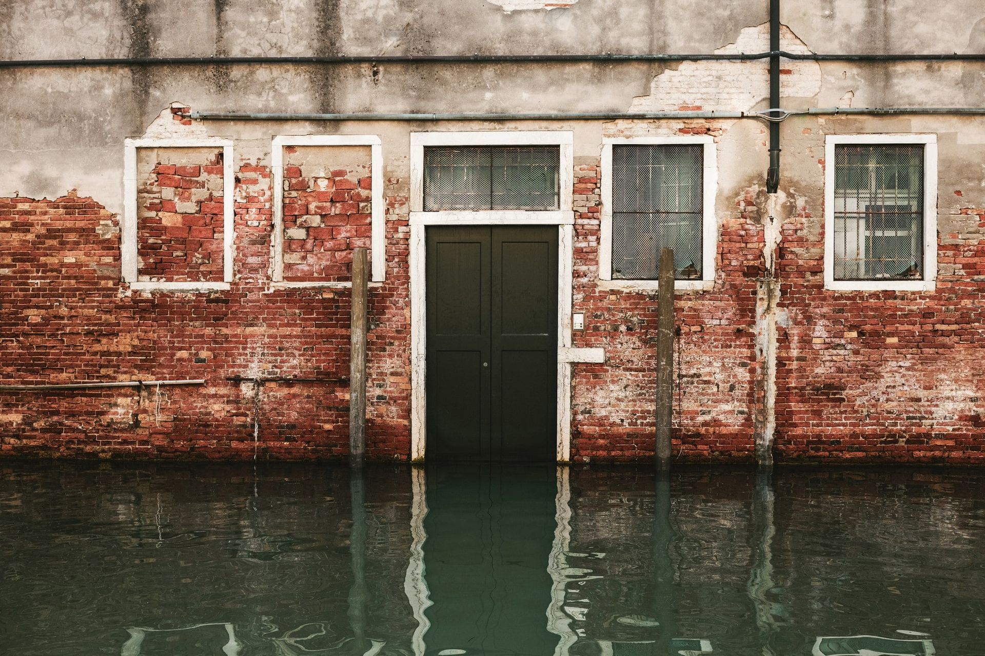 A brick building with a door and windows is surrounded by water.