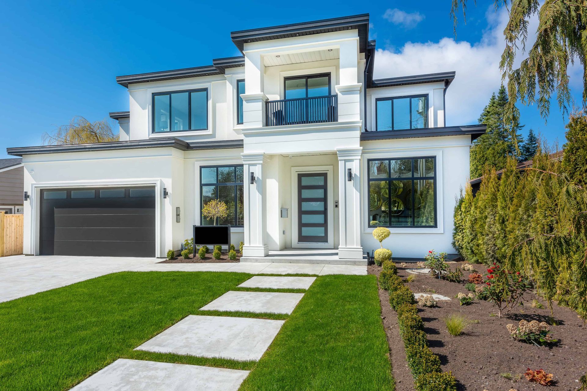 A large white house with a black garage door and a walkway leading to it.