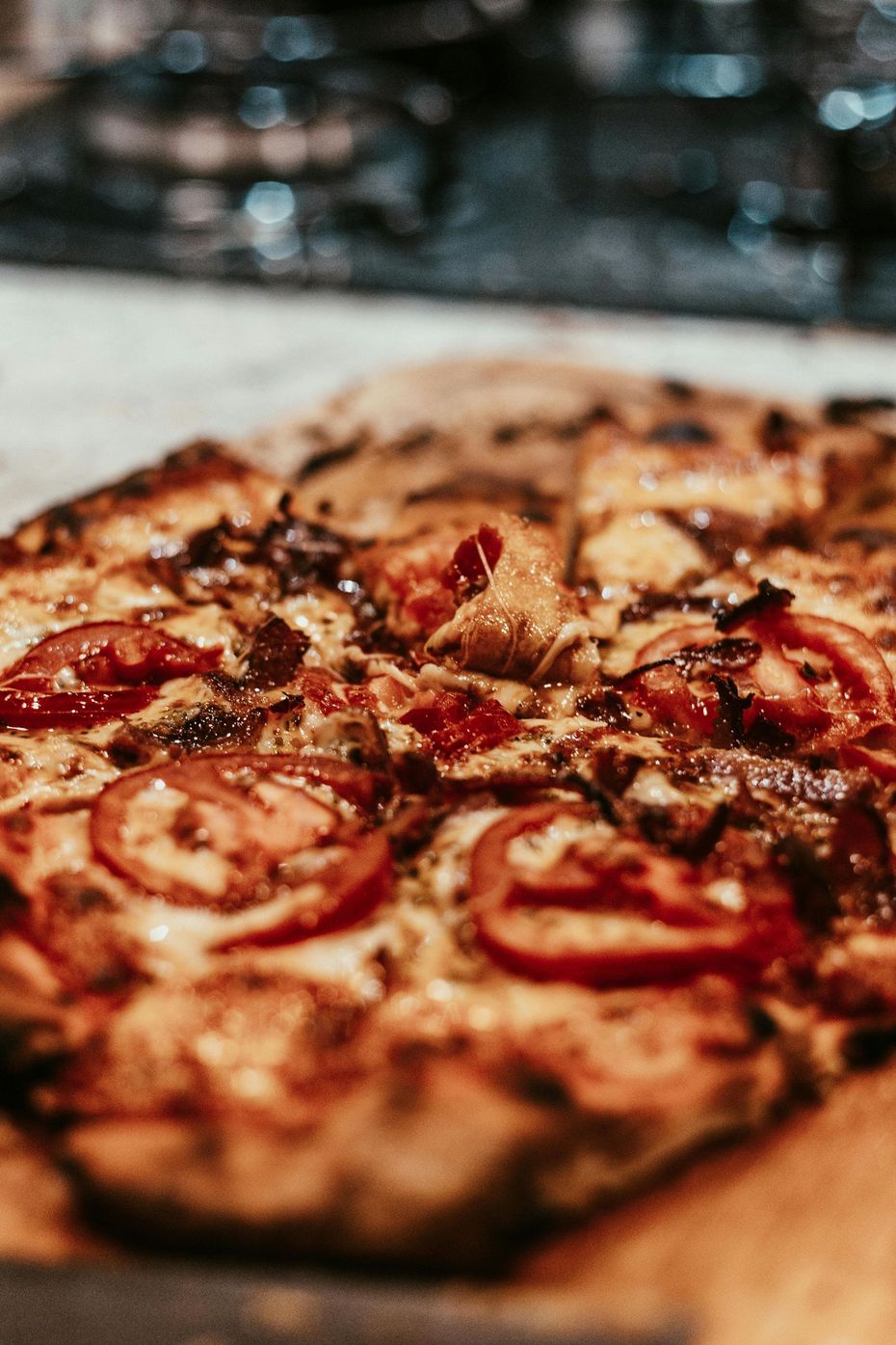 A rectangular pizza topped with sliced tomatoes, melted cheese, and dark herbs on a wooden board.