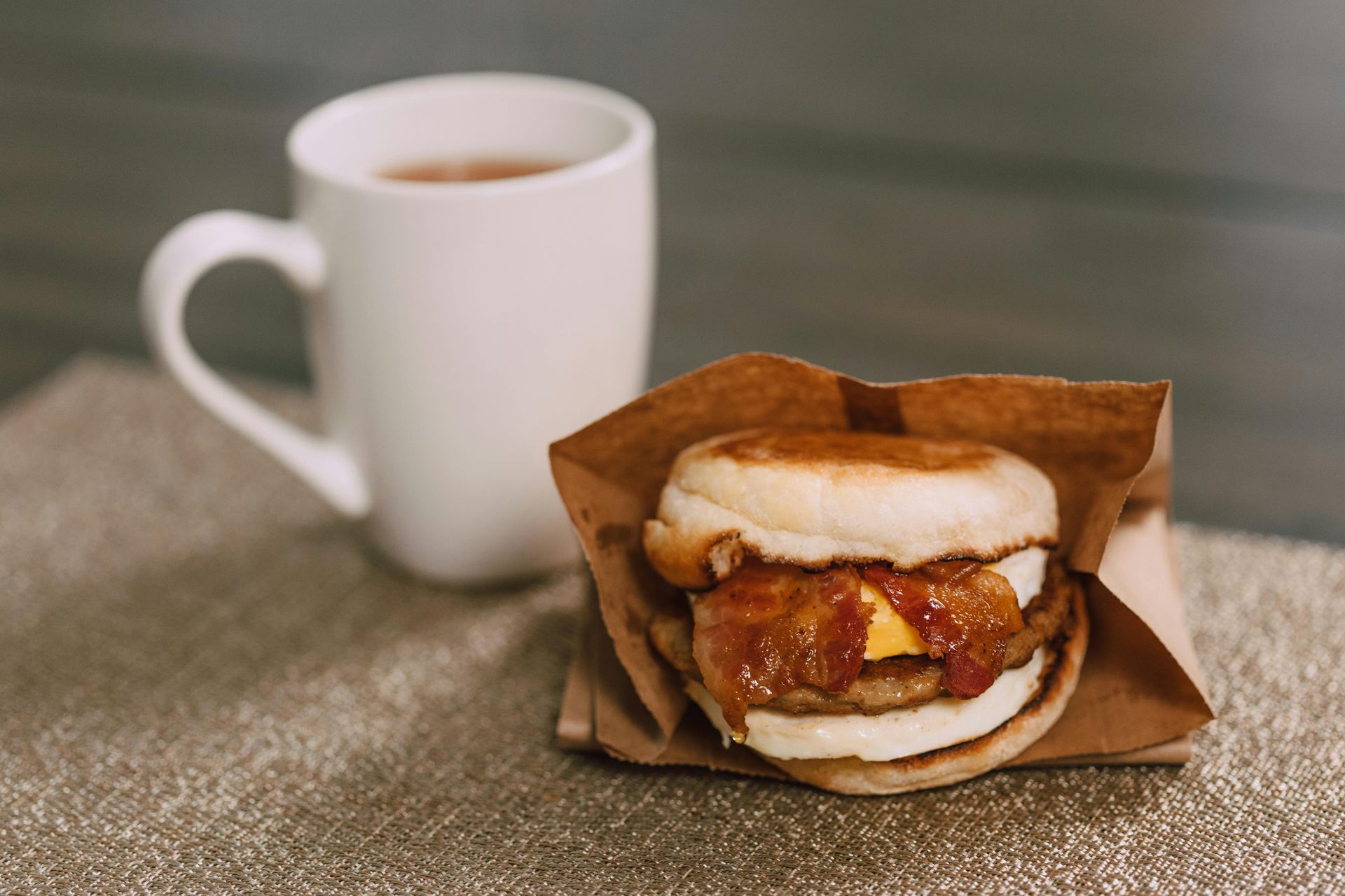 A white cup of espresso on a saucer, surrounded by scattered dark coffee beans and a burlap sack on a wooden table.