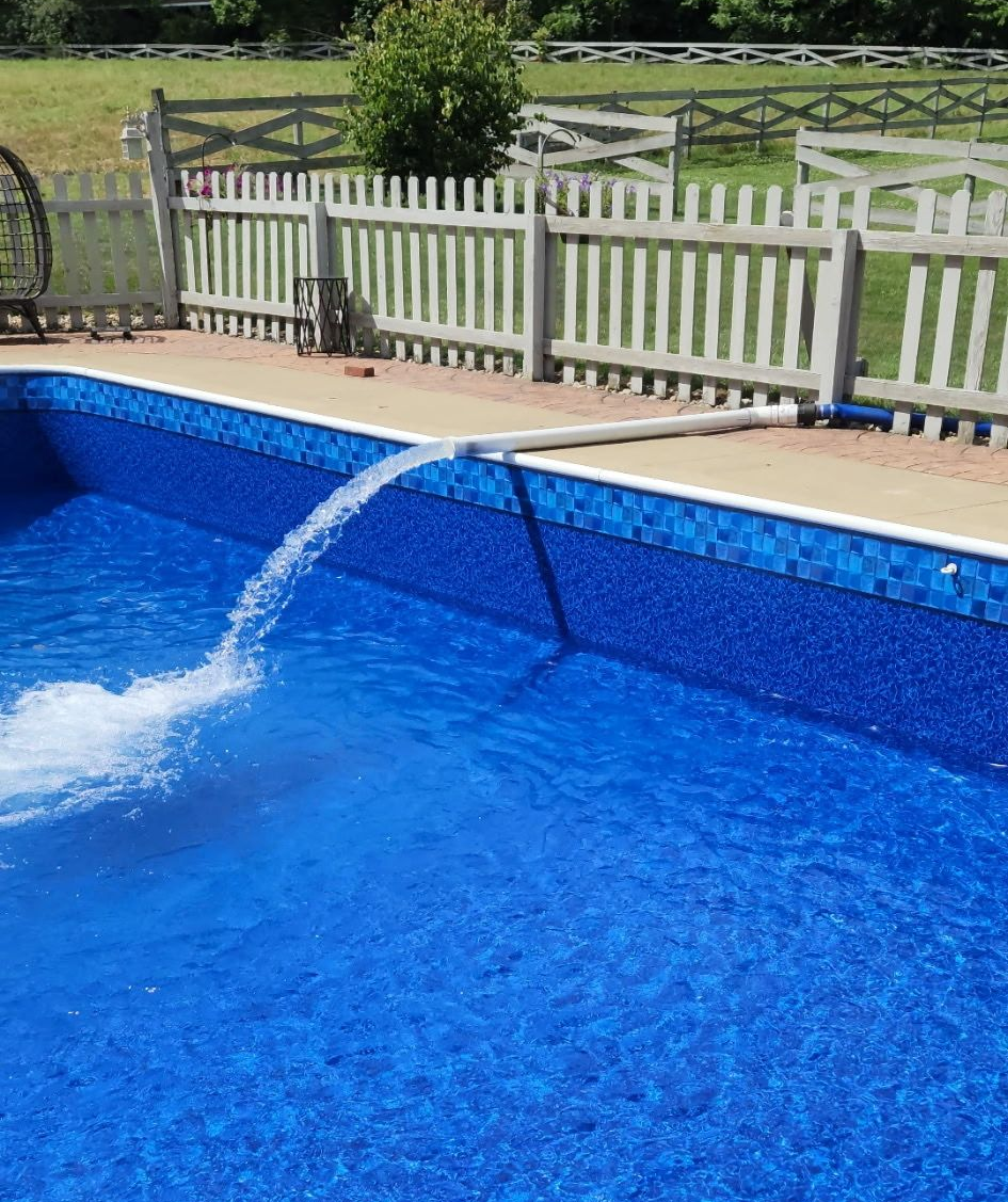 A swimming pool being filled with water from a white pipe; blue tile and fence in the background.