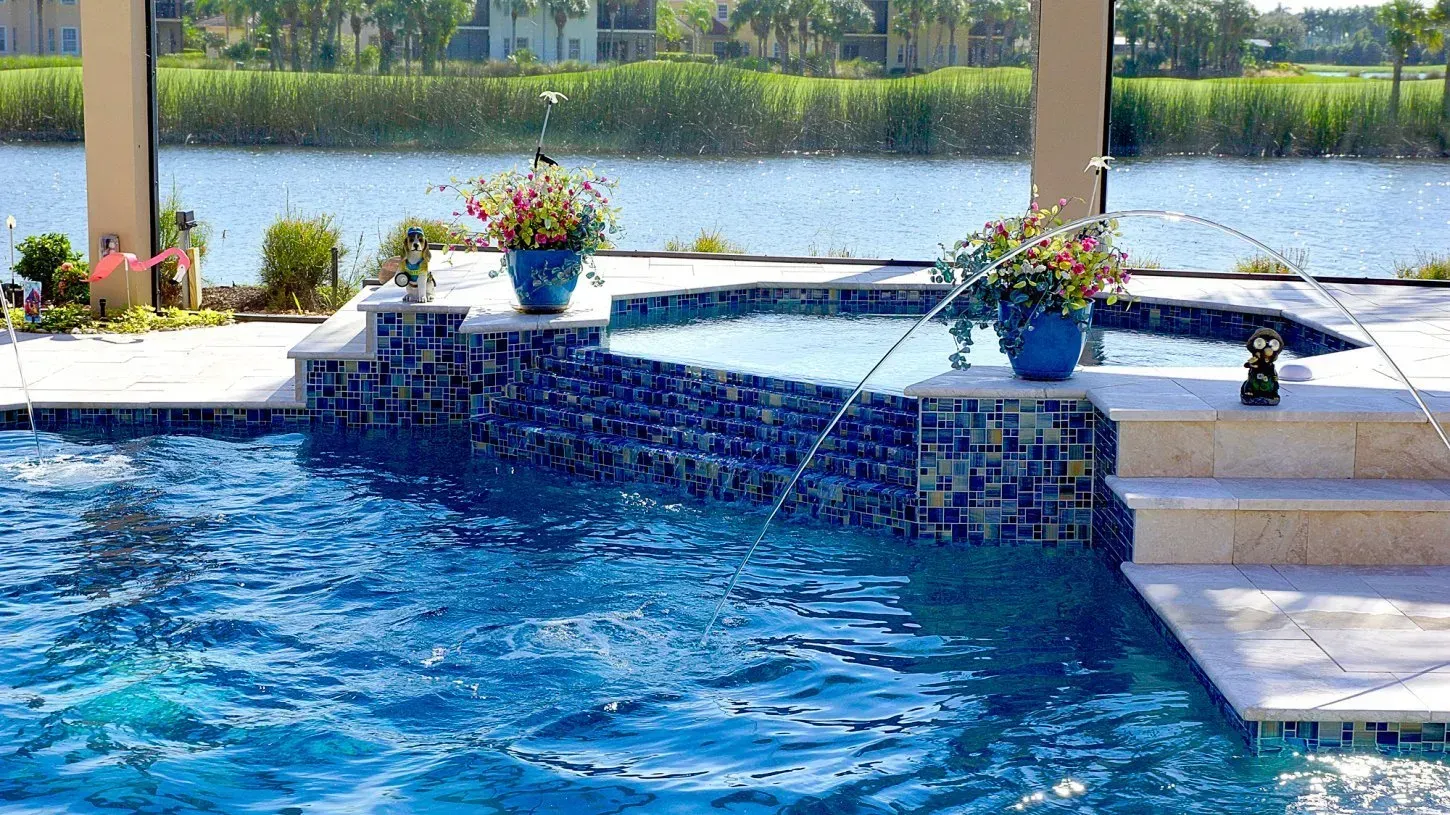 Pool with water features, hot tub, blue mosaic tile, and waterfront view.
