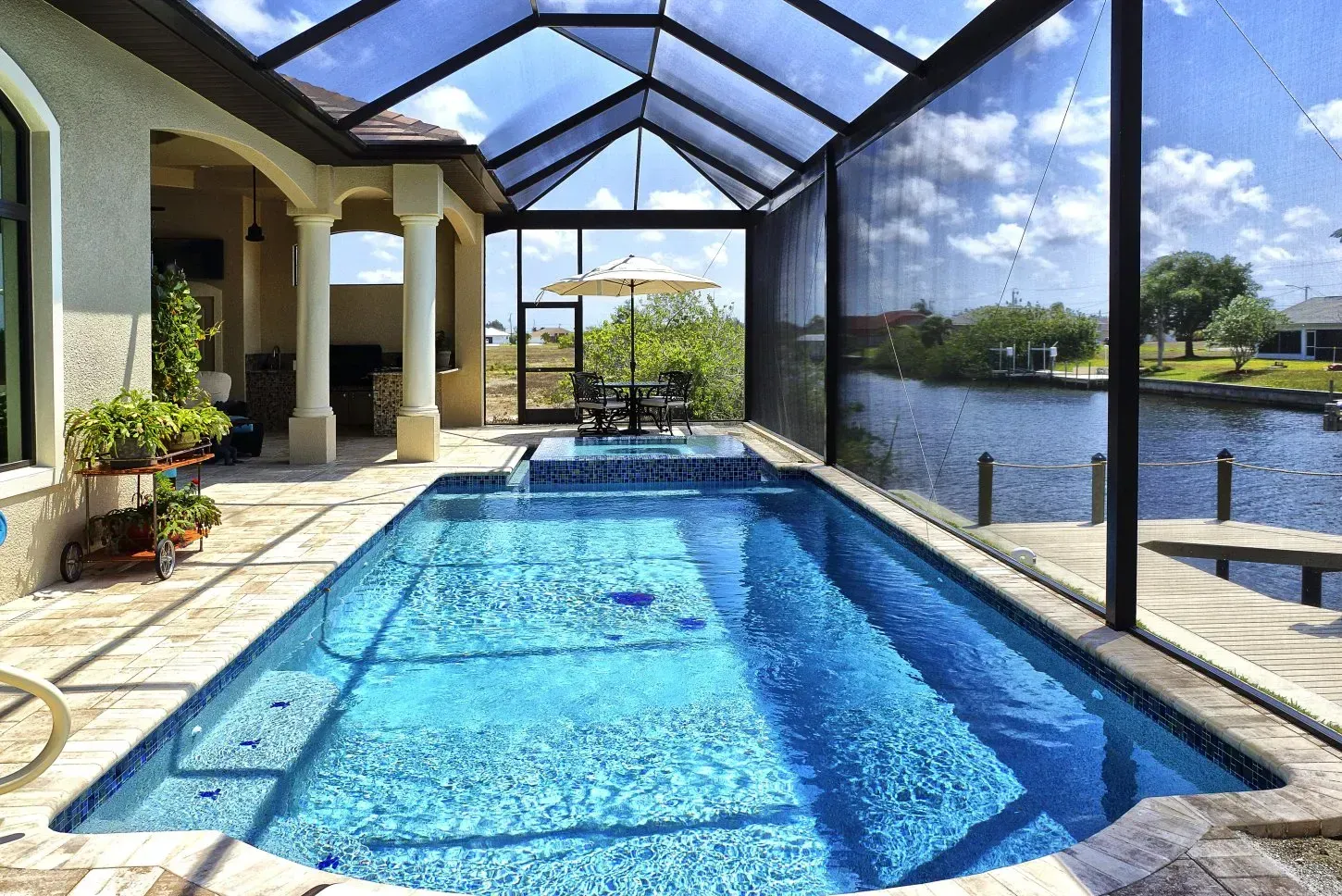 Swimming pool under screened enclosure next to a canal, sunny day.