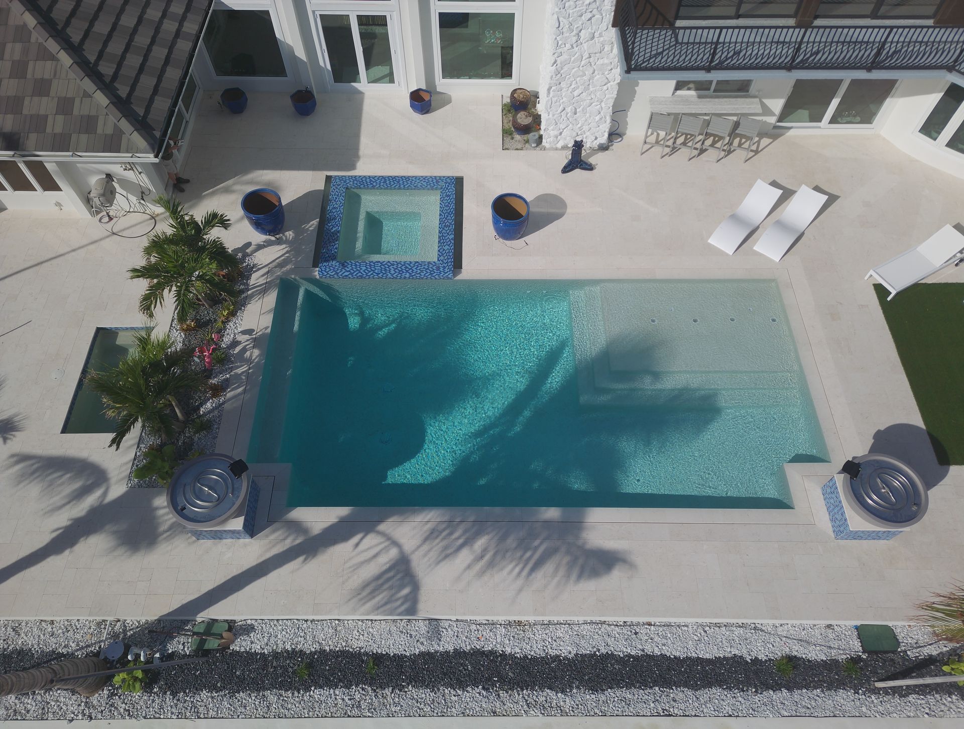 Overhead view of a luxury pool and hot tub in a modern home's backyard, with lounge chairs and landscaping.