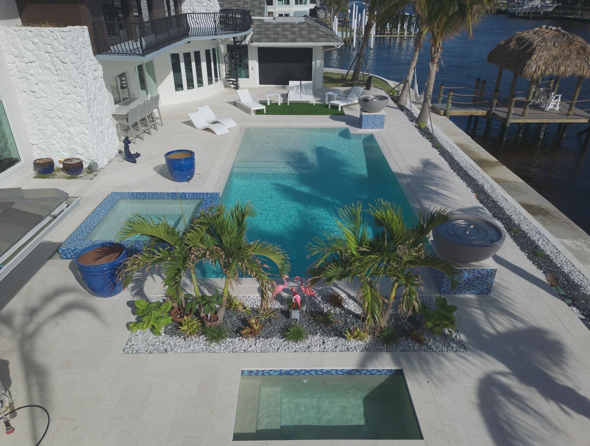Pool area with pool, spa, palm trees, and waterfront view.