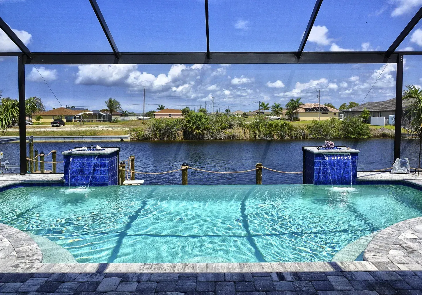 Pool with blue waterfall features overlooking a canal under a sunny sky.
