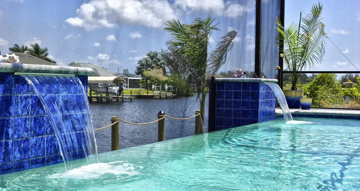 Blue tiled waterfalls into a pool, waterfront view, sunny day.