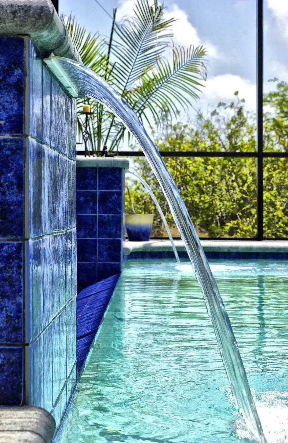 Blue tiled wall with water cascading into a pool, tropical setting.